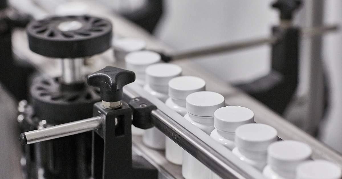 Close-up of a long production line machine processing many small white pill bottles without labels.